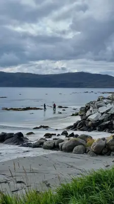 two people are standing in the water on the beach at Runde Miljøsenter & Opplev Runde in Runde