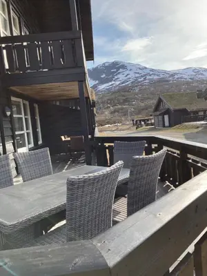 a wooden table and chairs on a deck with a mountain at Lun og koselig hytte med sauna på Filefjell in Tyinkrysset