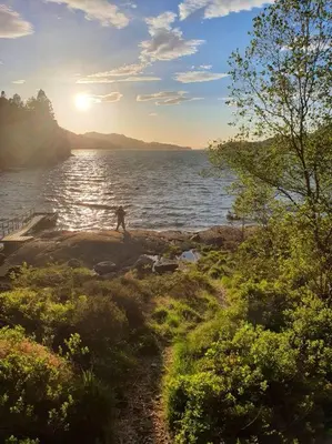 a person standing on the shore of a body of water at Nydelig leilighet- Solrik/2 balkonger in Seim