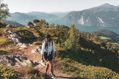 a woman walking on a hill overlooking a lake at Luxury Nordic Suite with Private Sauna and Panoramic Mountain Views in Stranda