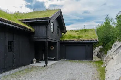 a black house with a grass roof with a garage at Luxurious 5-Bedroom Mountain Chalet with Sauna, Panoramic Views, and Two Full Bathrooms in Stranda