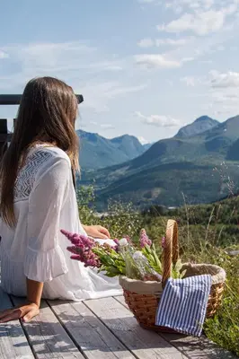 a woman sitting on a table with a basket of flowers at Luxurious 5-Bedroom Mountain Chalet with Sauna, Panoramic Views, and Two Full Bathrooms in Stranda