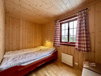 a bed in a wooden room with a window at Large cabin with Sjusjøens best view, sauna and ski in out in Ringsaker