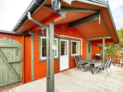 a red house with a wooden deck with a table and a barn at 6 person holiday home in Ånneland-By Traum in Ånneland