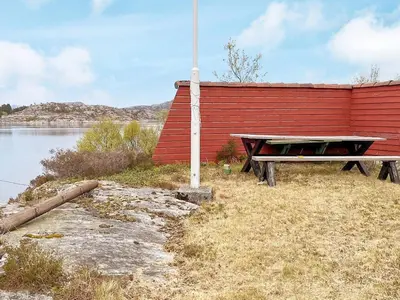 a picnic table next to a red building with a lake at 6 person holiday home in Ånneland-By Traum in Ånneland
