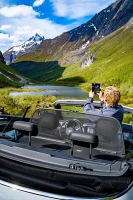 a person taking a picture of a mountain from a car at Ground Floor Exclusive Apartment with Sauna - Near Geiranger and the Norwegian Fjords in Stranda