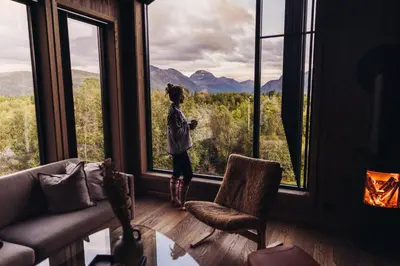 a girl standing in a room looking out of a window at Nordic Luxury Apartment - Private Sauna & Panoramic Mountain Views in Stranda