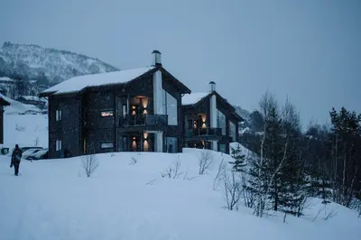 a large house in the snow with a person walking in front at Nordic Luxury Apartment - Private Sauna & Panoramic Mountain Views in Stranda