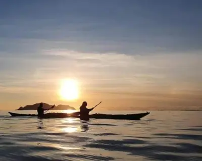 two people in a canoe in the water at sunset at Beach front appartments in design eco-villa in Ulsteinvik