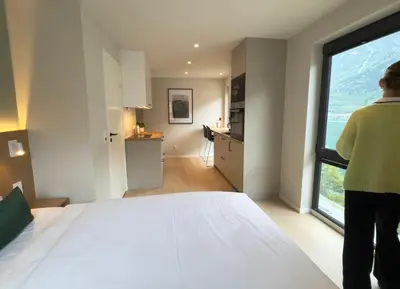 a woman standing in a bedroom looking out the window at Odda City Apartments in Odda