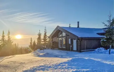 a house on a snowy hill with the sun in the background at Beautiful Home In Sjusjøen With Sauna in Sjusjøen