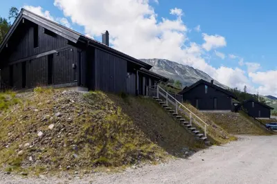 a black building on a hill next to a dirt road at Hovdetunet 77-Gaustablikk in Gaustablikk