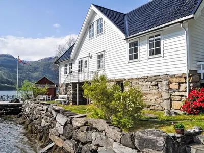 a white house with a stone wall next to the water at Holiday Home Ørviksnes by Interhome in Steinstø