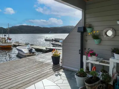 a deck with potted plants and a house on the water at Apartment Heningen by Interhome in Uggdal