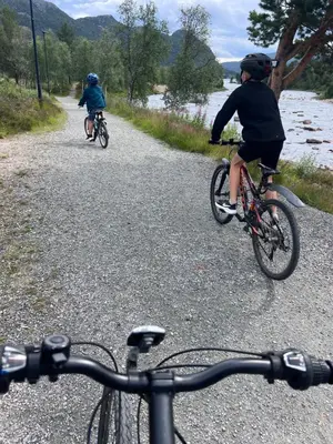 two people riding bikes on a gravel road next to a river at Solsetra - Mountain Majesty Family Log Cabin in Hovden