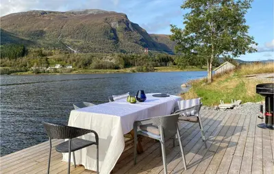 a table and chairs on a deck next to a lake at 2 Bedroom Cozy Home In Straumgjerde in Riksem