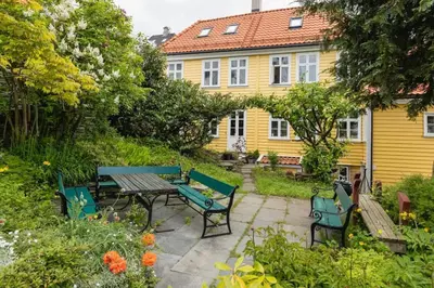 a garden with benches and a yellow house at Dinbnb Apartments I Historical Two-Floor Apartment with Rooftop Panorama I 1645 Heritage in Bergen