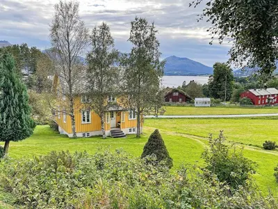 a yellow house on a green field with mountains in the background at 6 person holiday home in AVERØY-By Traum in Stein