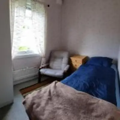 a bedroom with a bed and a chair and a window at Feriehus Voldstad in Syvde