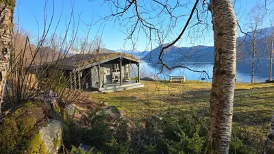 a small building in a field next to a lake at Bregnehytte in Leikanger