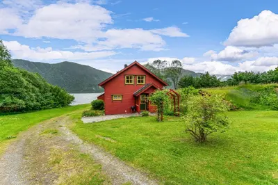 a red house in the middle of a green field at Fjord Lodge direkt am Ufer des Dalsfjord in Lauvstad
