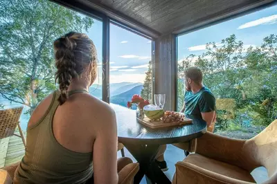 a woman sitting at a table looking out a window at a man at Sørheim FjordPanorama in Skjolden