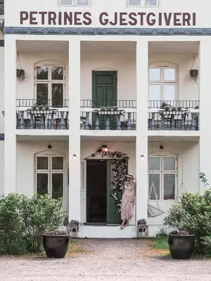 a facade of a white building with a woman in a pink dress at Petrines Gjestgiveri in Norddal