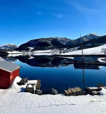 a lake with snow and a red building and a boat at Hus ved Valsøyfjorden in Otnes