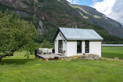 a small white house in a field with a mountain at Jordeplegarden holiday home - Part of a farm - Two buildings - Close to Flåm in Lærdalsøyri