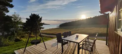 a wooden deck with a table and chairs on it at Strandstua Solbakken Feriehus in Fevåg