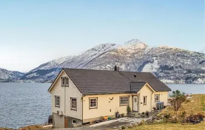 a house by the water with mountains in the background at 4 Bedroom Awesome Home In Tørvikbygd in Tyrvikbygd