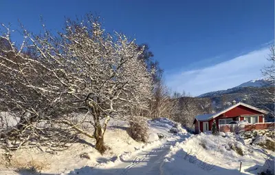 a snow covered tree next to a red cabin at Lovely Home In Bjordal With Kitchen in Bjordal