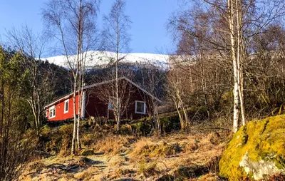 a red cabin in the woods with a snow covered mountain at Lovely Home In Bjordal With Kitchen in Bjordal