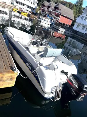 a white boat is docked at a dock at Rorbu i Austevoll med 3 soverom og mulighet for båtleie in Kolbeinsvik