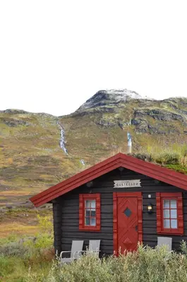 a small cabin with a red door on a hill at Tyinholmen Høyfjellsstuer in Eidsbugarden