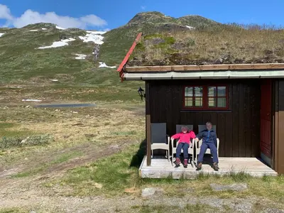 two people sitting on the porch of a house at Tyinholmen Høyfjellsstuer in Eidsbugarden