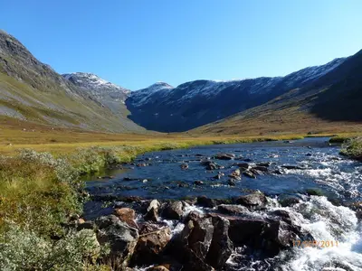 a river in a field with mountains in the background at Hole Hytter in Geiranger