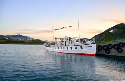 a white boat is docked next to a dock at Fagerstrand, storhytte ved Bygdin i Jotunheimen in Beitostøl