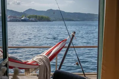 a person sitting in a hammock on a boat on the water at New! Sea front apt. with terrace above the sea! in Bergen