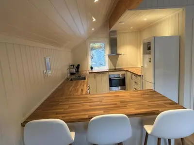 a kitchen with a counter with white chairs in it at Rorbu i Gilsvågen - Egen Brygge - Båtutleie in Blænes