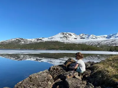 a woman sitting on rocks fishing on a lake at Ladebua in Brunstad