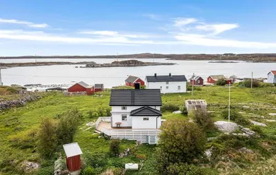 a group of houses in a field with a body of water at Cozy Home In Norddyrøy With Kitchen in Sætra