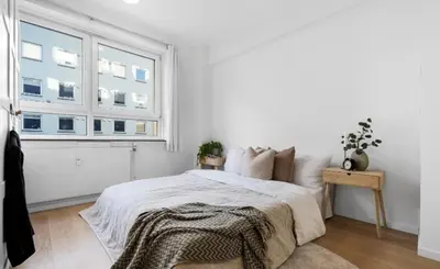 a white bedroom with a bed and a window at Nydelig leilighet på Nordnes! in Bergen