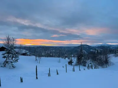 a snow covered field with trees and a sunset at Eventyrtunet in idyllic Tuddal in Hjartdal