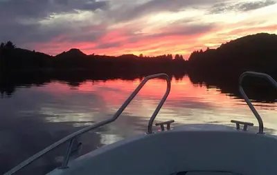 a boat on a lake with a sunset in the background at 3 Bedroom Stunning Home In Bøvågen in Bøvågen