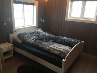 a bed in a bedroom with two windows at Hytte med god standard in Stranda