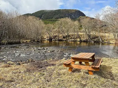 a wooden picnic table sitting next to a river at 4 person holiday home in Lysøysundet in Teksdal