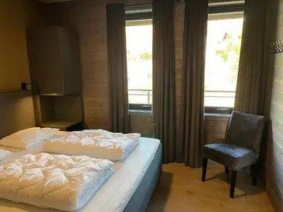 a bedroom with two beds and a chair and windows at Riddertunets utsikt til Slettefjell in Beitostøl