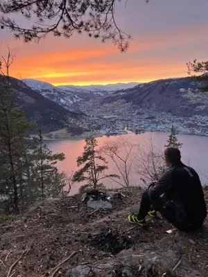 a man sitting on top of a hill looking at a lake at Studio apartment in Sogndal