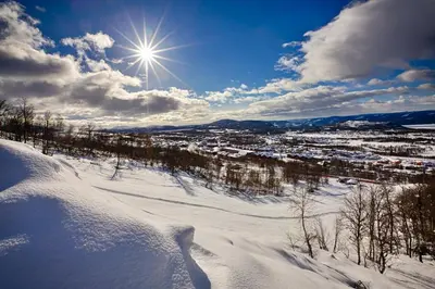 a snow covered slope with the sun in the sky at Bright and Modern penthouse apartment in Beitostøl